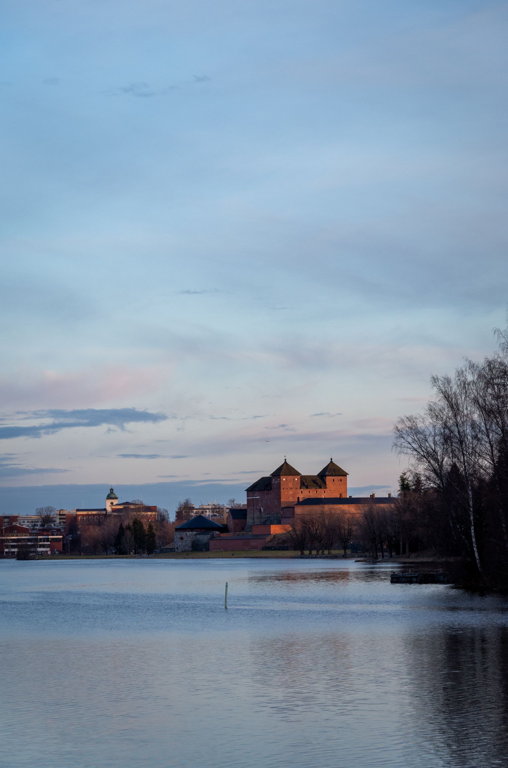 Peaceful sunset view of Hämeenlinna Castle with a lake in the foreground, Finland.